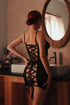 A person wearing a black, sheer dress with an open lace-up back standing in a bathroom setting.
